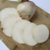Close-up of a sliced Purple Top White Globe turnip on a wooden cutting board, showing the crisp white interior of several round slices fanned out in front of the root.