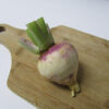 Purple Top White Globe turnip with trimmed green tops resting on a wooden cutting board, showing its classic two-tone root with a smooth white bottom and vibrant purple shoulders.