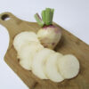 Purple Top White Globe turnip displayed on a wooden cutting board, with the whole root standing upright and several round slices arranged neatly in front, revealing its crisp white interior.