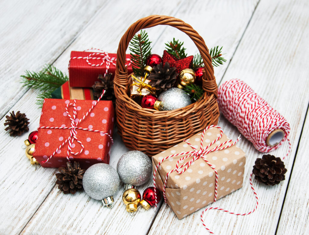 Wicker basket filled with Christmas decorations and gifts surrounded by pinecones.