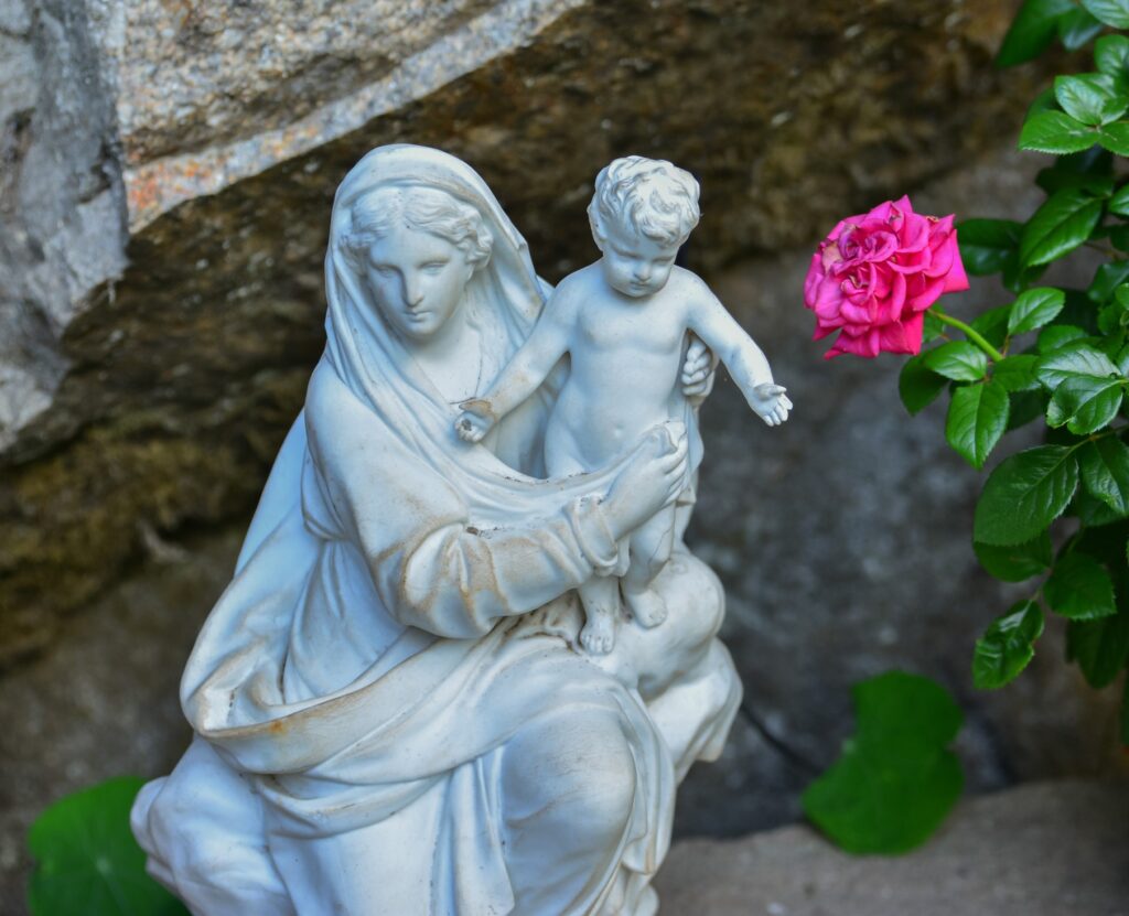 Marian statue with the Child Jesus next to a single bright rose, representing the gentle, prayerful spirit of a Mary Garden.