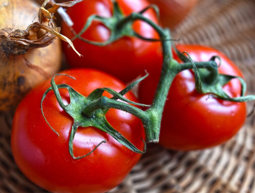Fresh vine tomatoes resting beside an onion on a woven surface.